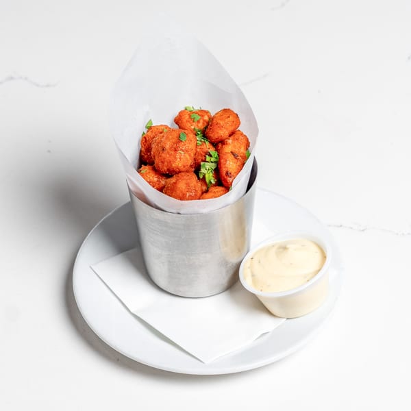 Crispy orange Pear Street Bistro tots with green herbs in a metal cup, served with a side of dipping sauce.
