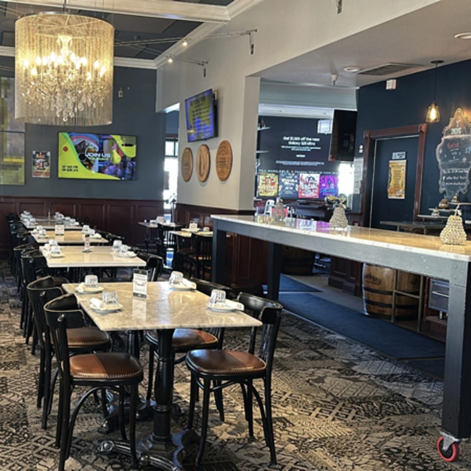 Interior of Pear Street Bistro with dining tables, chairs, a bar, and a large chandelier.