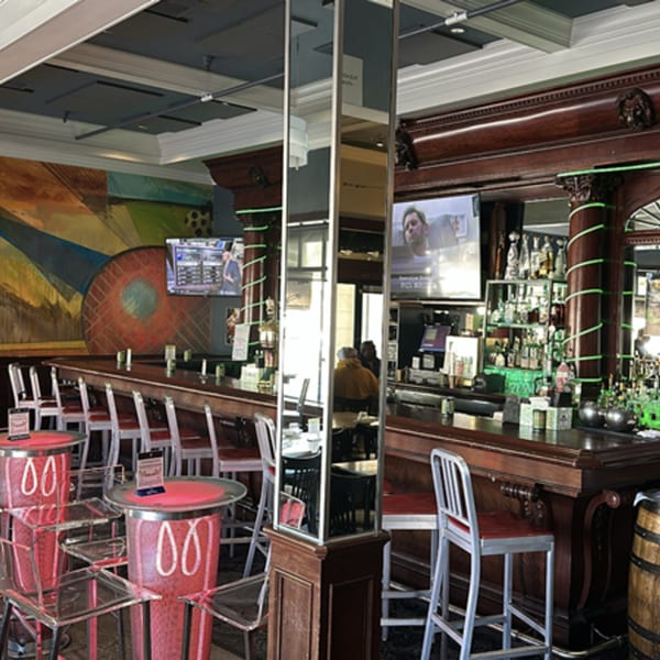 Interior of Pear Street Bistro bar with dark wood, red stools, and a colorful mural.