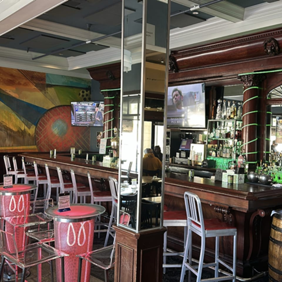 Interior of Pear Street Bistro bar with dark wood, red stools, and a colorful mural.