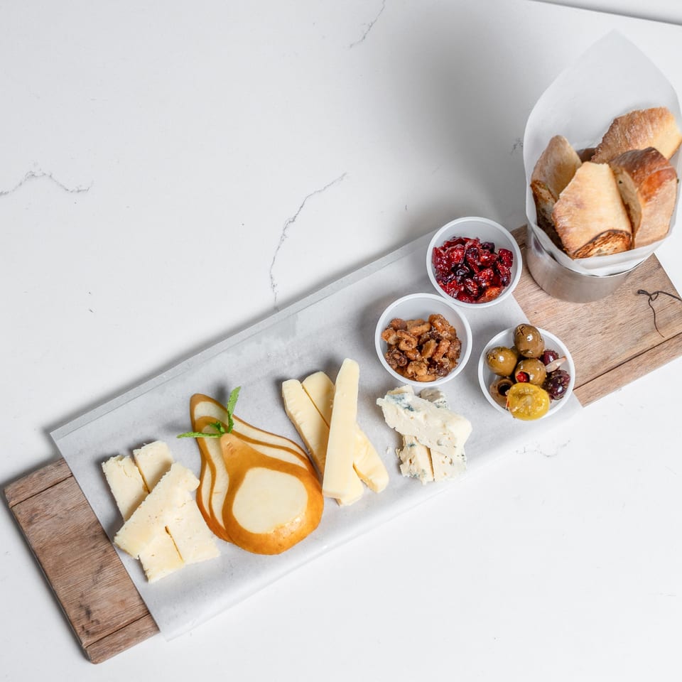 A charcuterie board with cheeses, candied pear, olives, nuts, dried cranberries, and bread.
