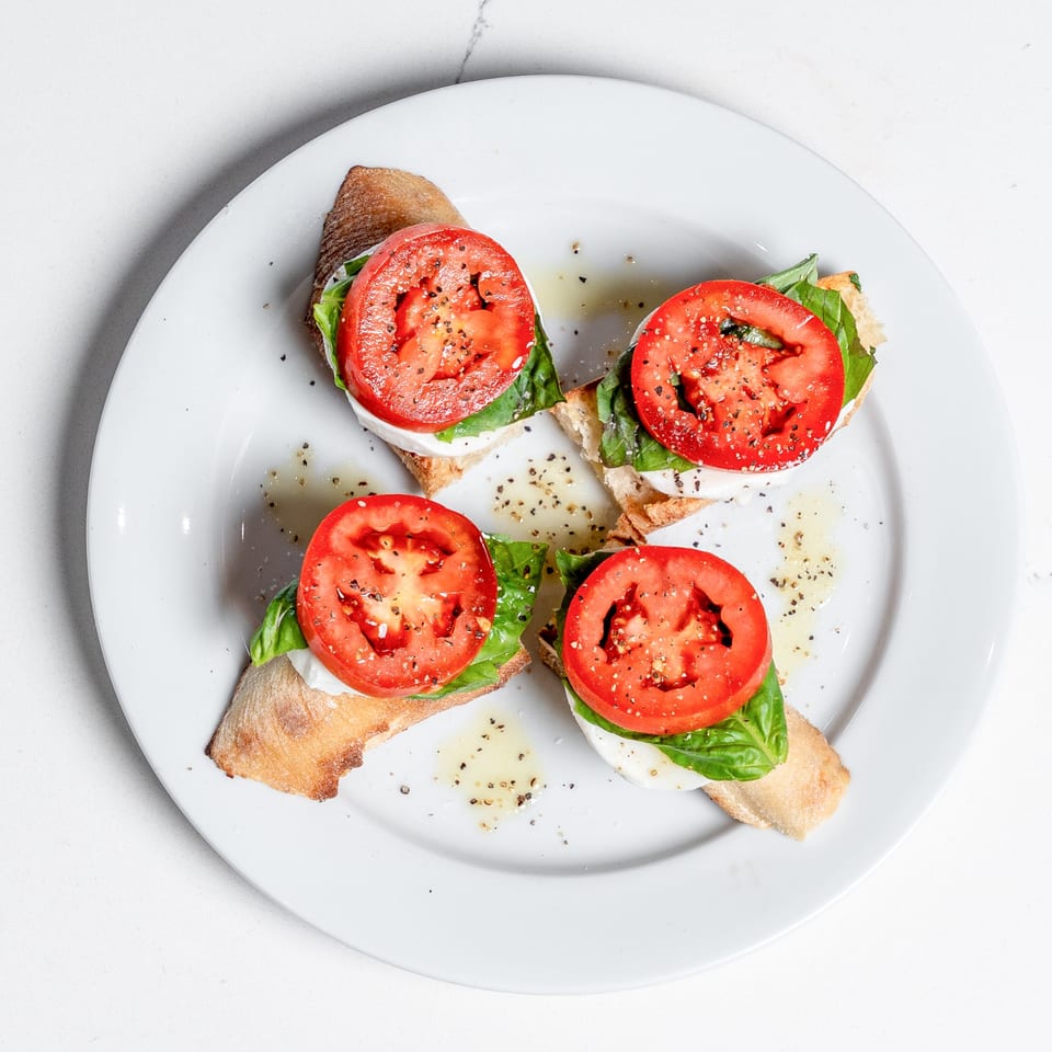 Four bruschetta pieces with tomato, mozzarella, basil, and pepper on a white plate.