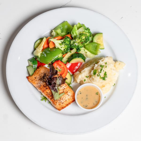 Pear Street Bistro's salmon entree with mashed potatoes, mixed vegetables, and a side of sauce.