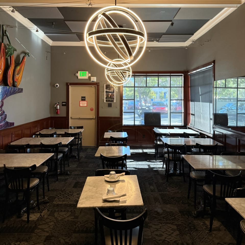 The Pear Street Bistro dining room features marble tables, dark chairs, and glowing orb chandeliers.
