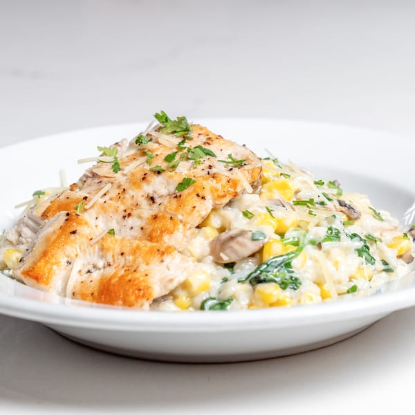 Pan-seared chicken breast over creamy risotto with corn, mushrooms, spinach, and grated cheese.